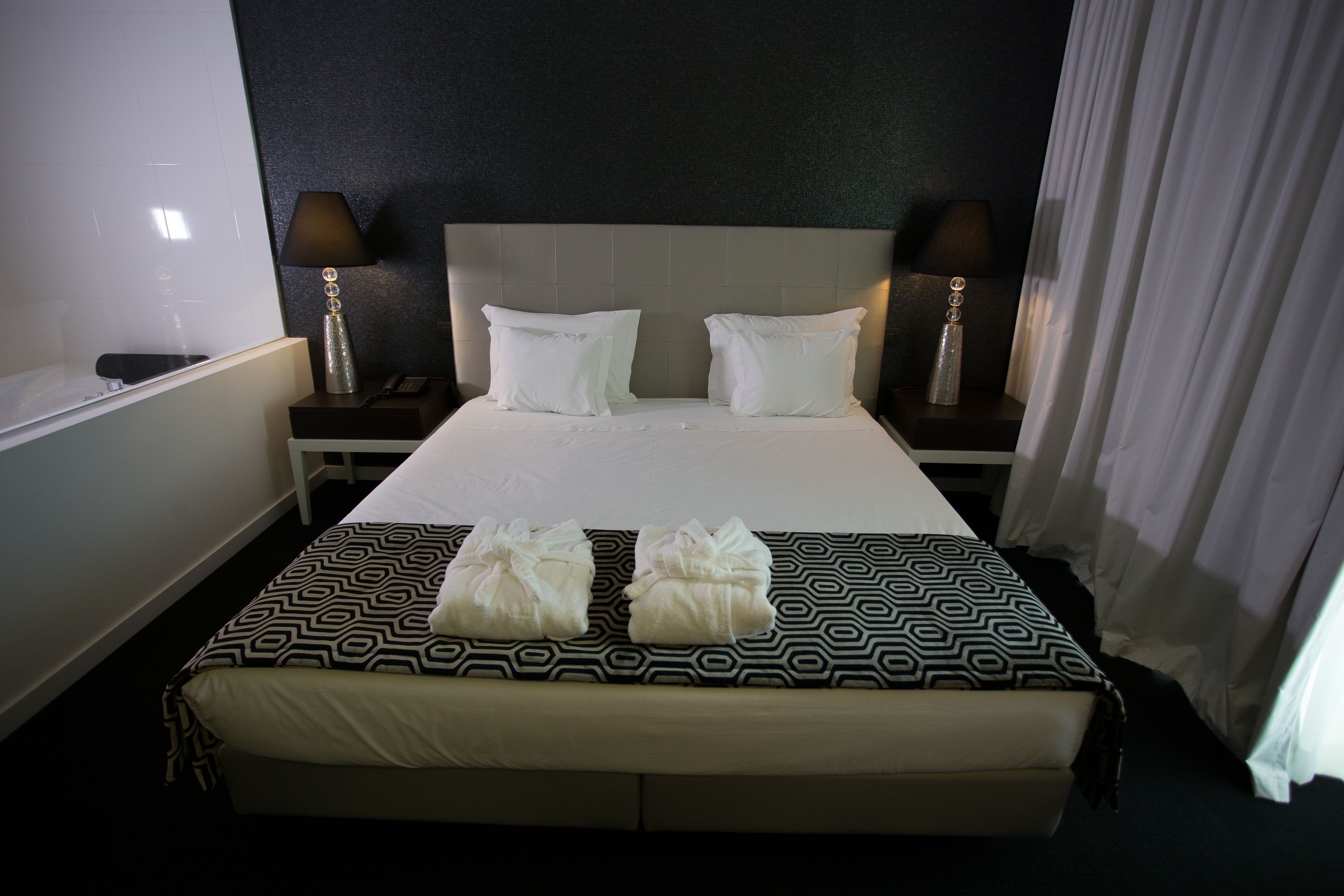 A hotel room with a large bed, two bedside tables, a nightstand, a lamp, and a curtain.