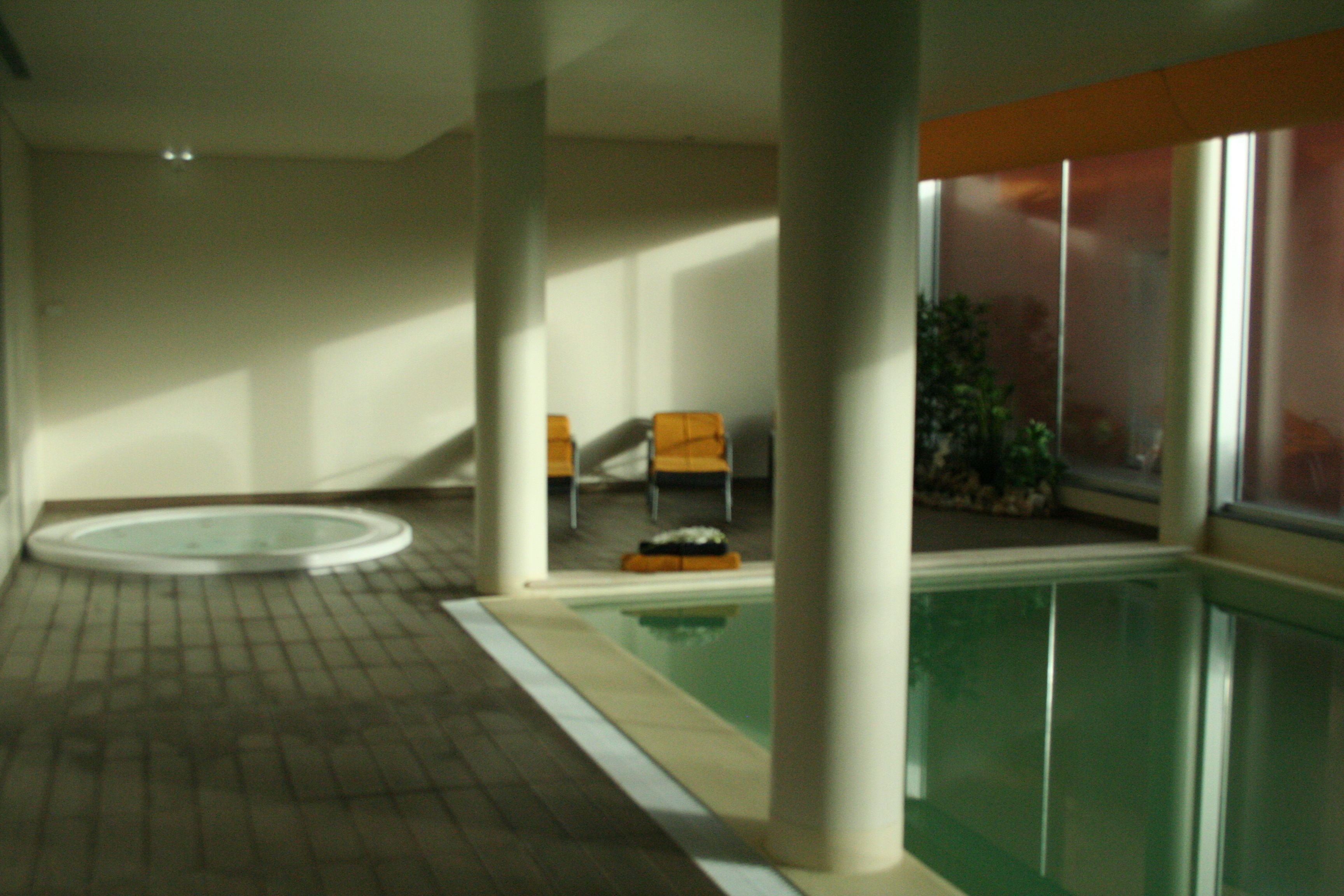 An indoor swimming pool with tiled flooring, a few lounge chairs, and a glass partition wall.