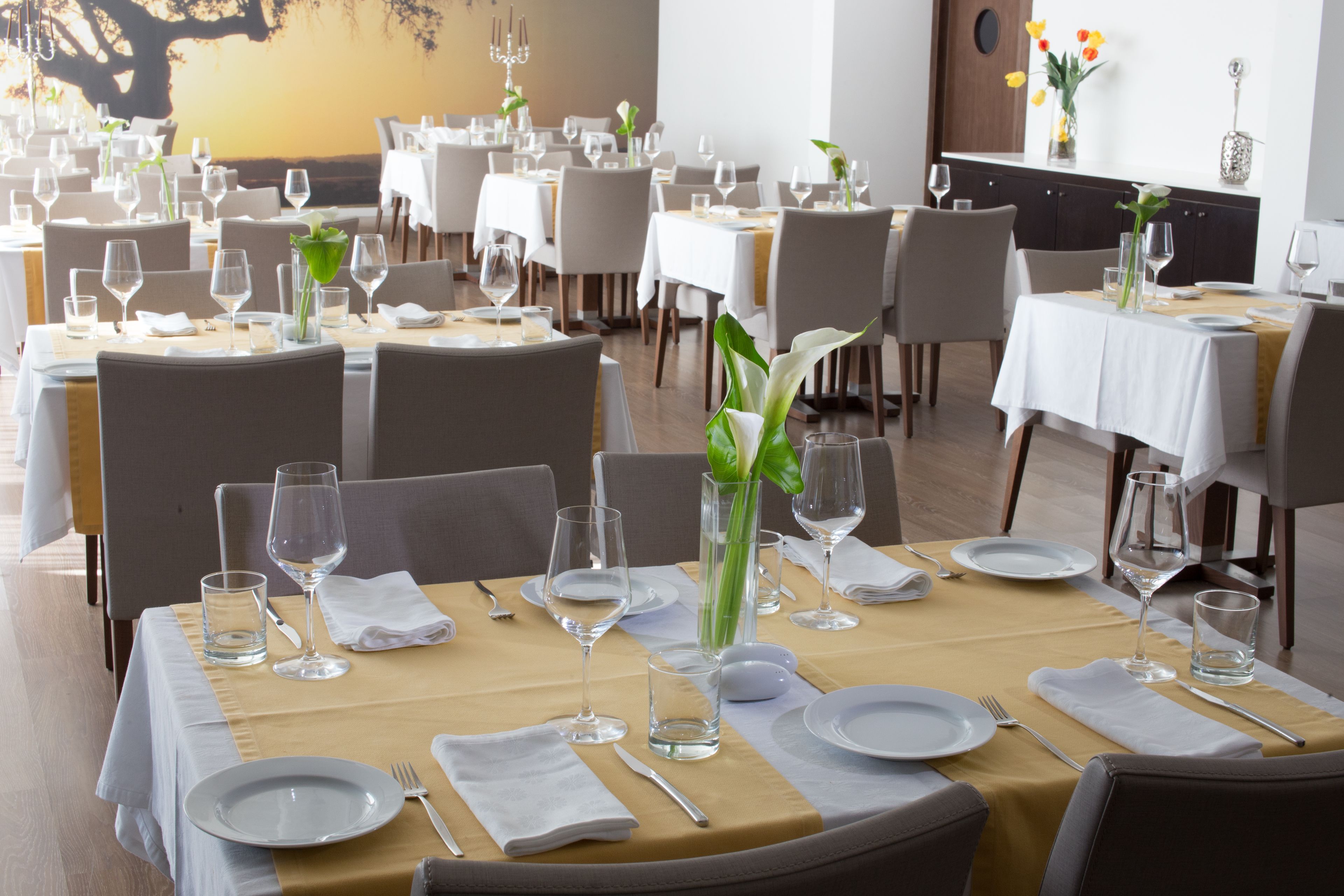 Un restaurant avec de nombreuses tables dressées pour le service, chacune étant équipée d’assiettes, de couverts et de verres.