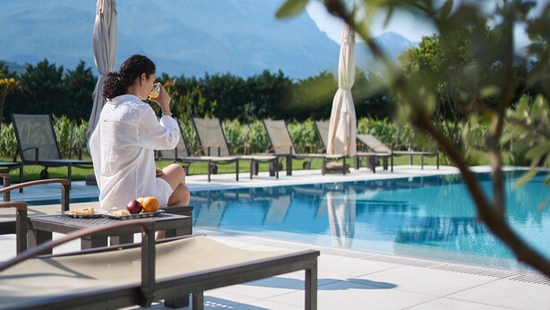 A person sitting by a poolside with a mountain view in the background. - Albergo Al Maso (Riva del Garda)