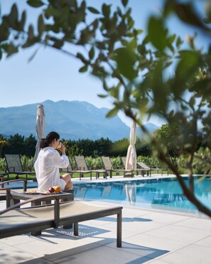 Une personne assise au bord d’une piscine, avec une vue sur les montagnes en arrière-plan.