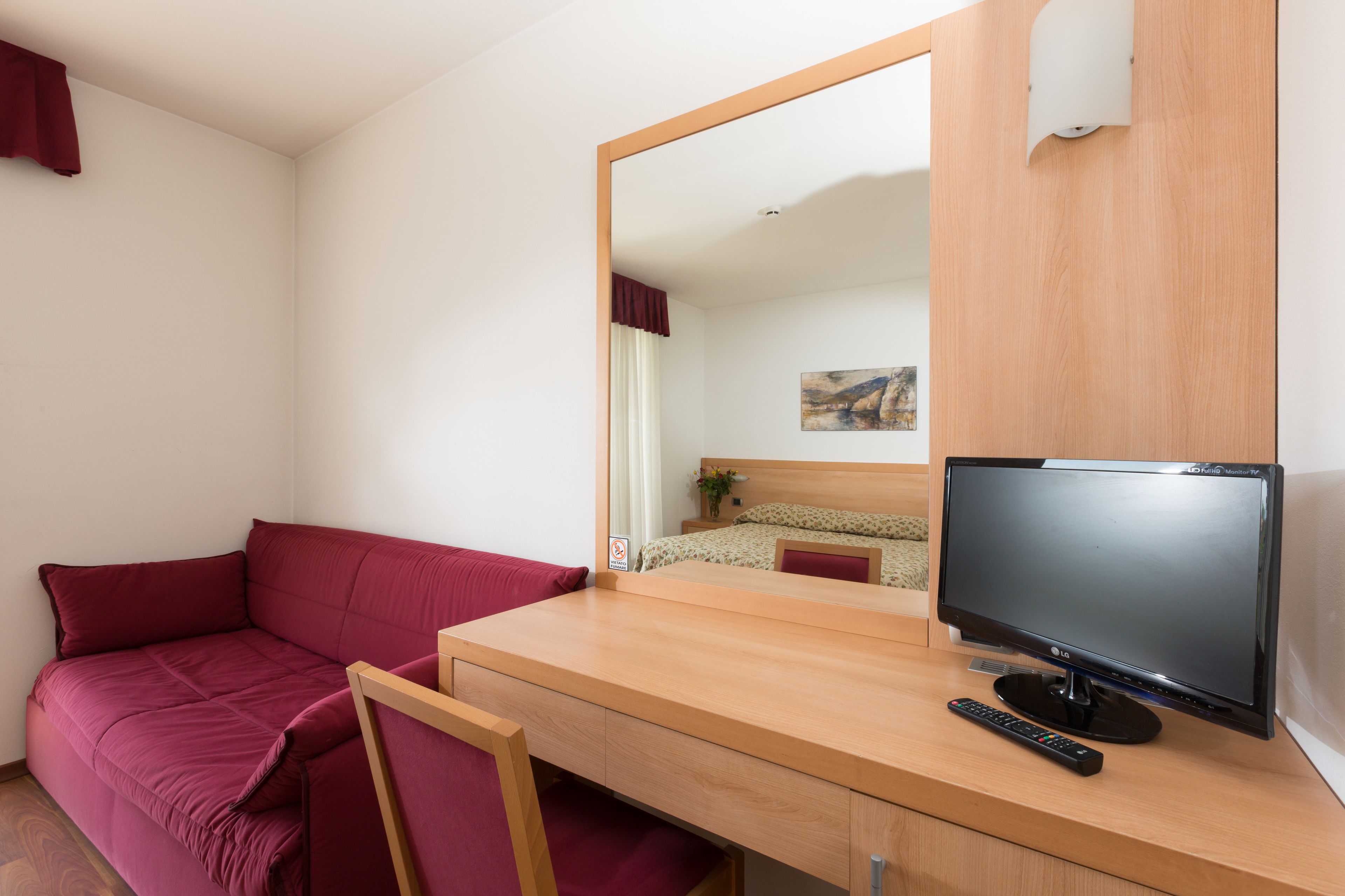Ein Zimmer mit einem Holztisch, einem Fernseher, einem roten Sofa und einem Spiegel.