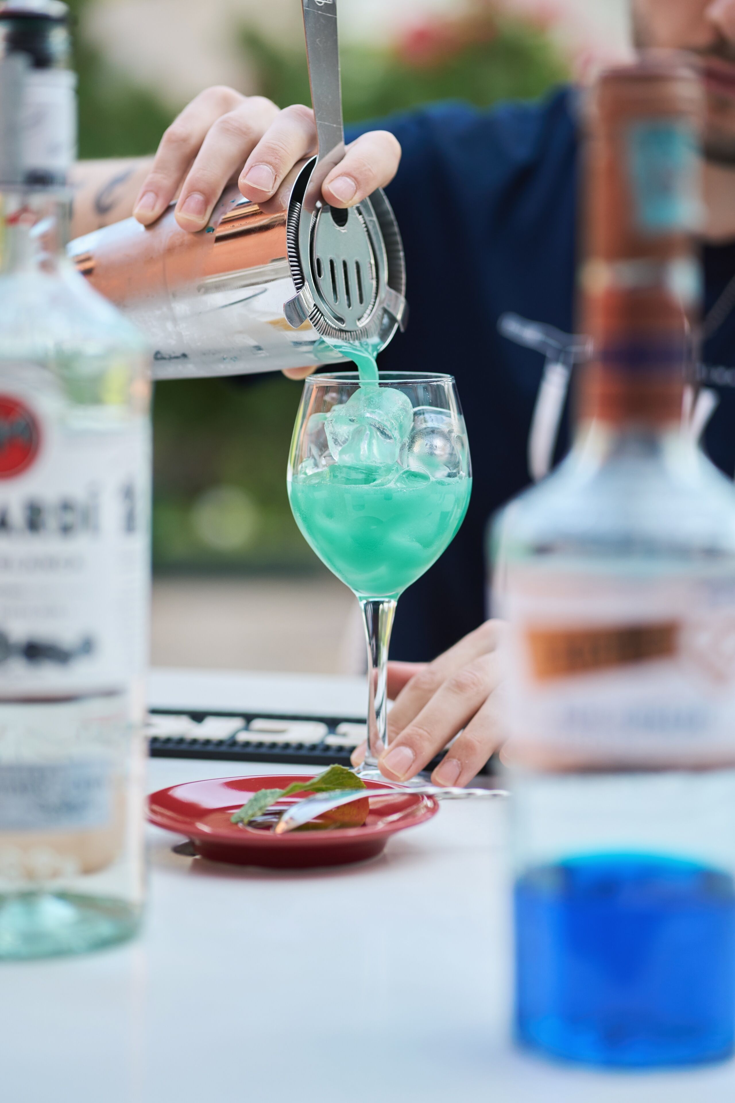 A person pouring a green liquid into a glass with a metal strainer.