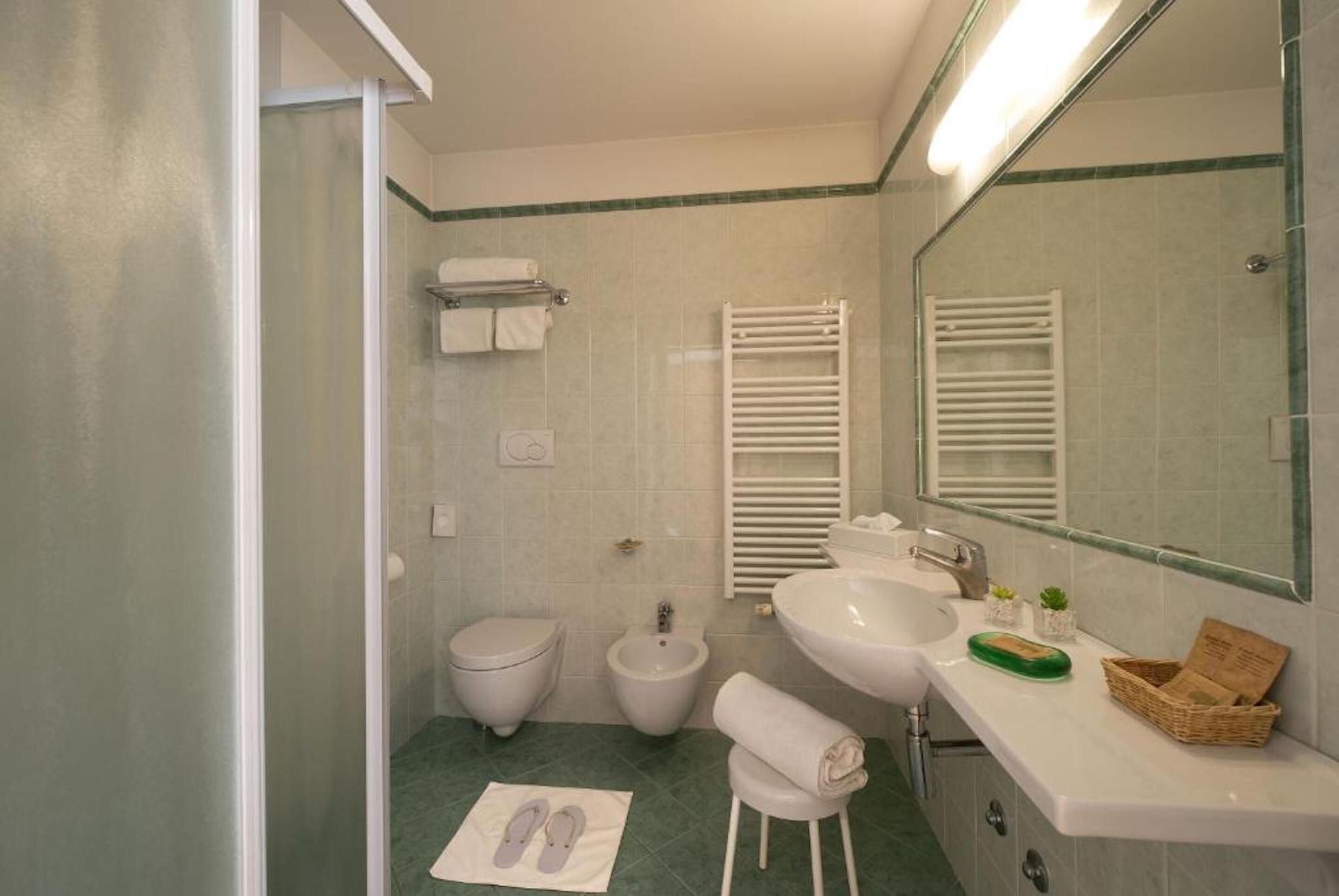 A bathroom with a toilet, bidet, sink, and mirror. There are towels and a basket on the counter.