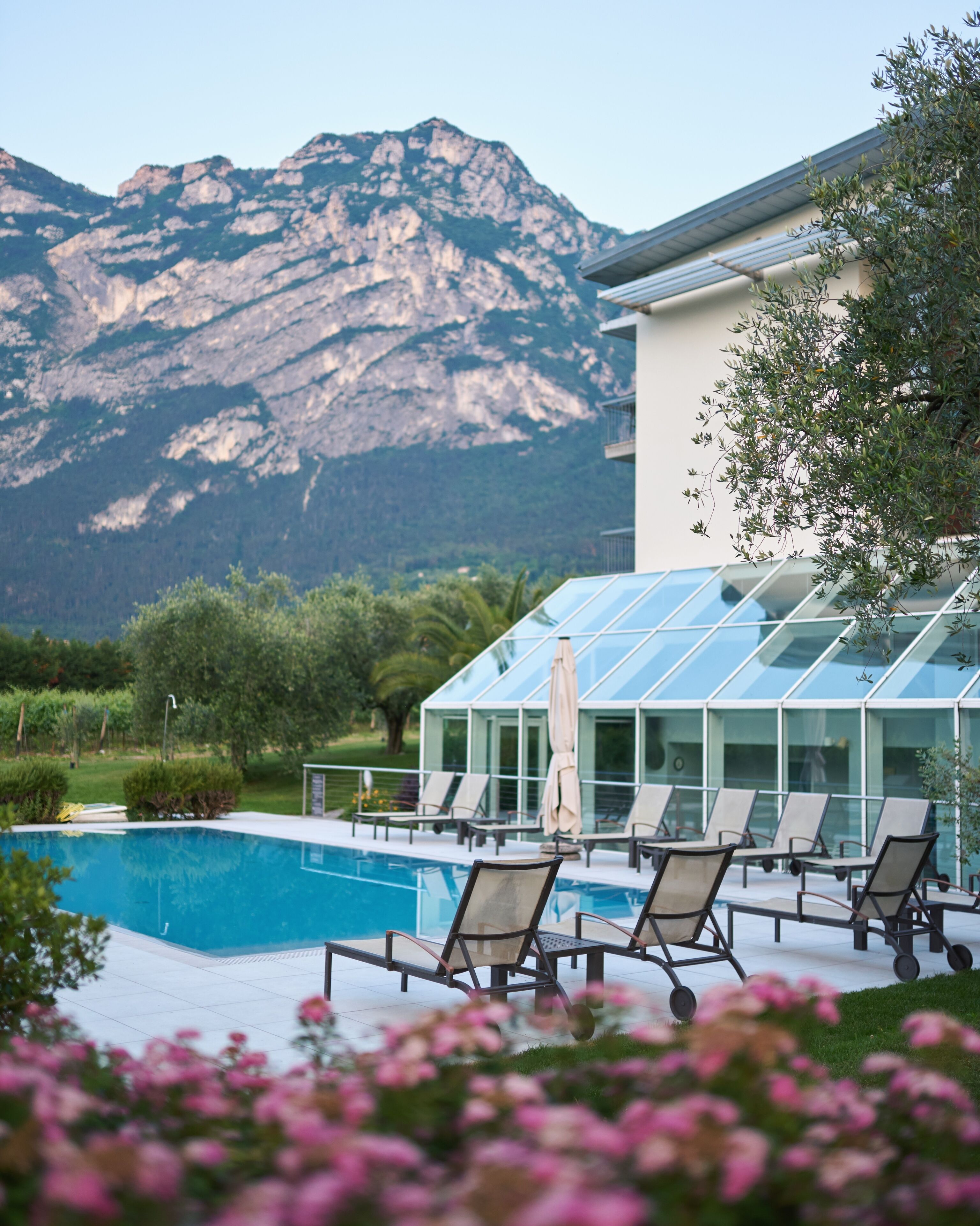 A pool area with lounge chairs and a glass-enclosed structure, set against a mountain backdrop.