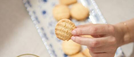 A hand holding a cookie, a glass of orange juice, and a plate with cookies in the background.