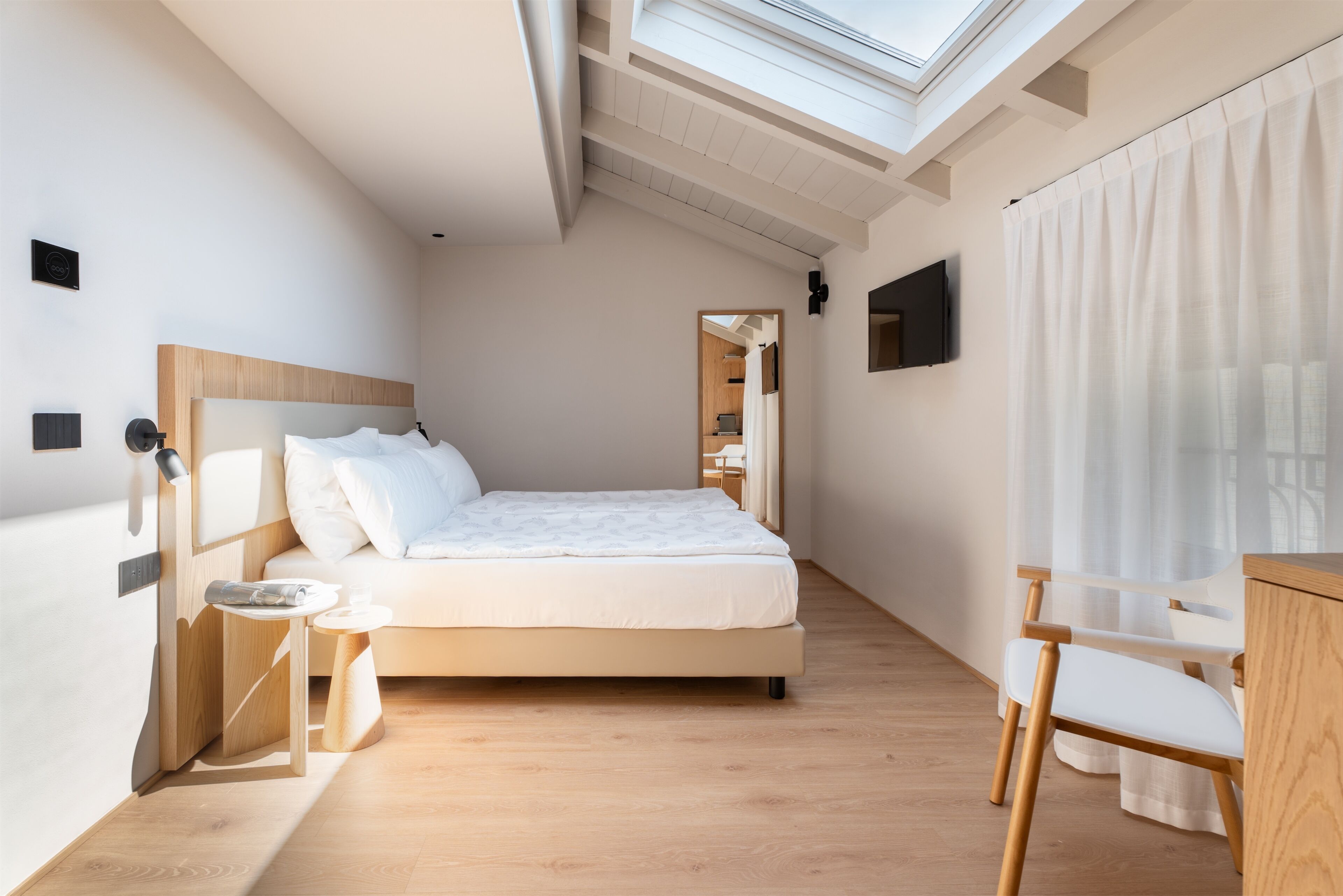 Une chambre moderne avec un puits de lumière, un lit, une table de chevet, une chaise et un téléviseur fixé au mur.