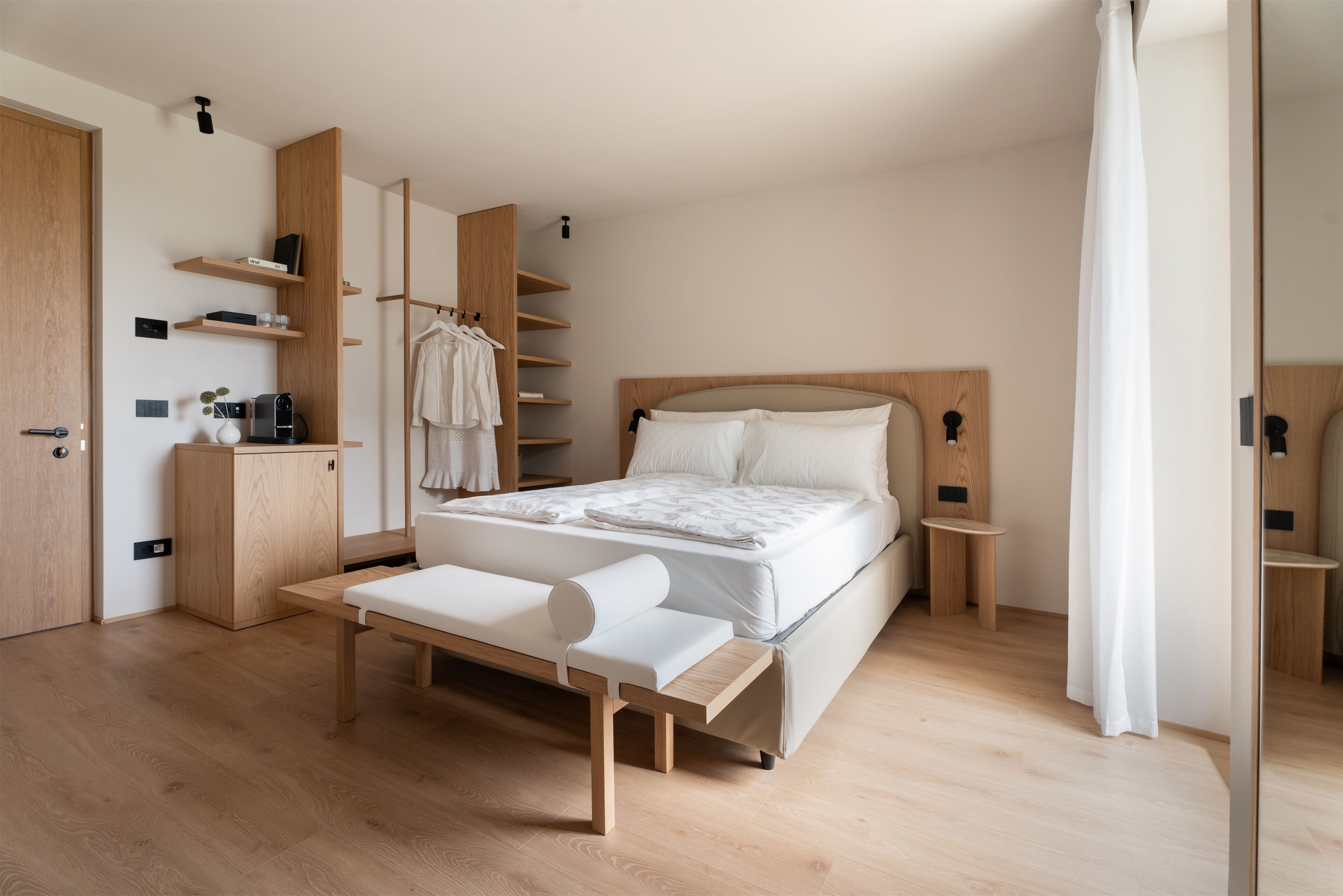 Een moderne slaapkamer met een houten bed, inbouwkasten, een nachtkastje en een bankje.