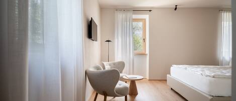 A bedroom with a bed, a chair, a small table, and a window with curtains.