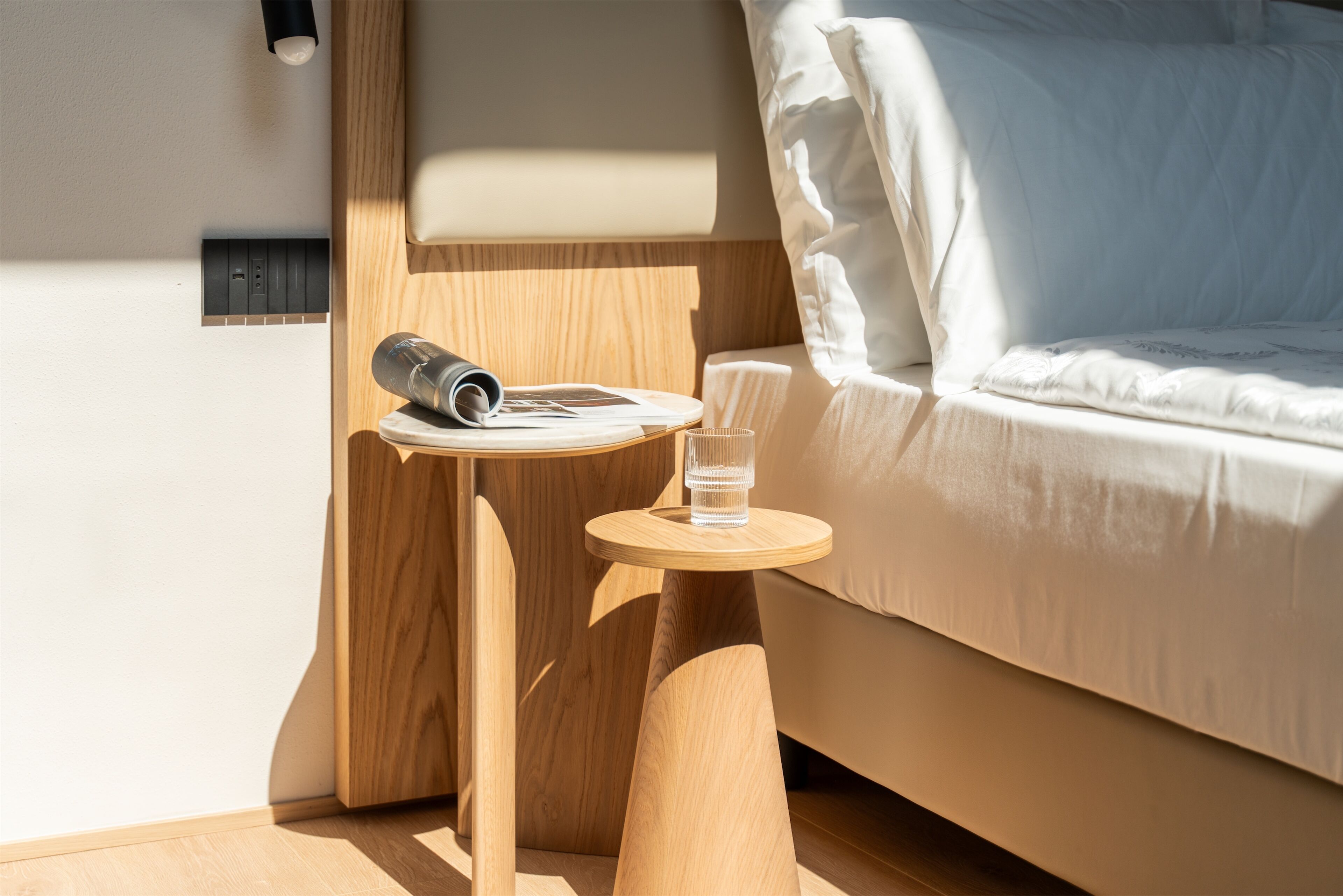 A neatly arranged hotel room with a bed, a small wooden side table, a glass of water, and a rolled-up towel.