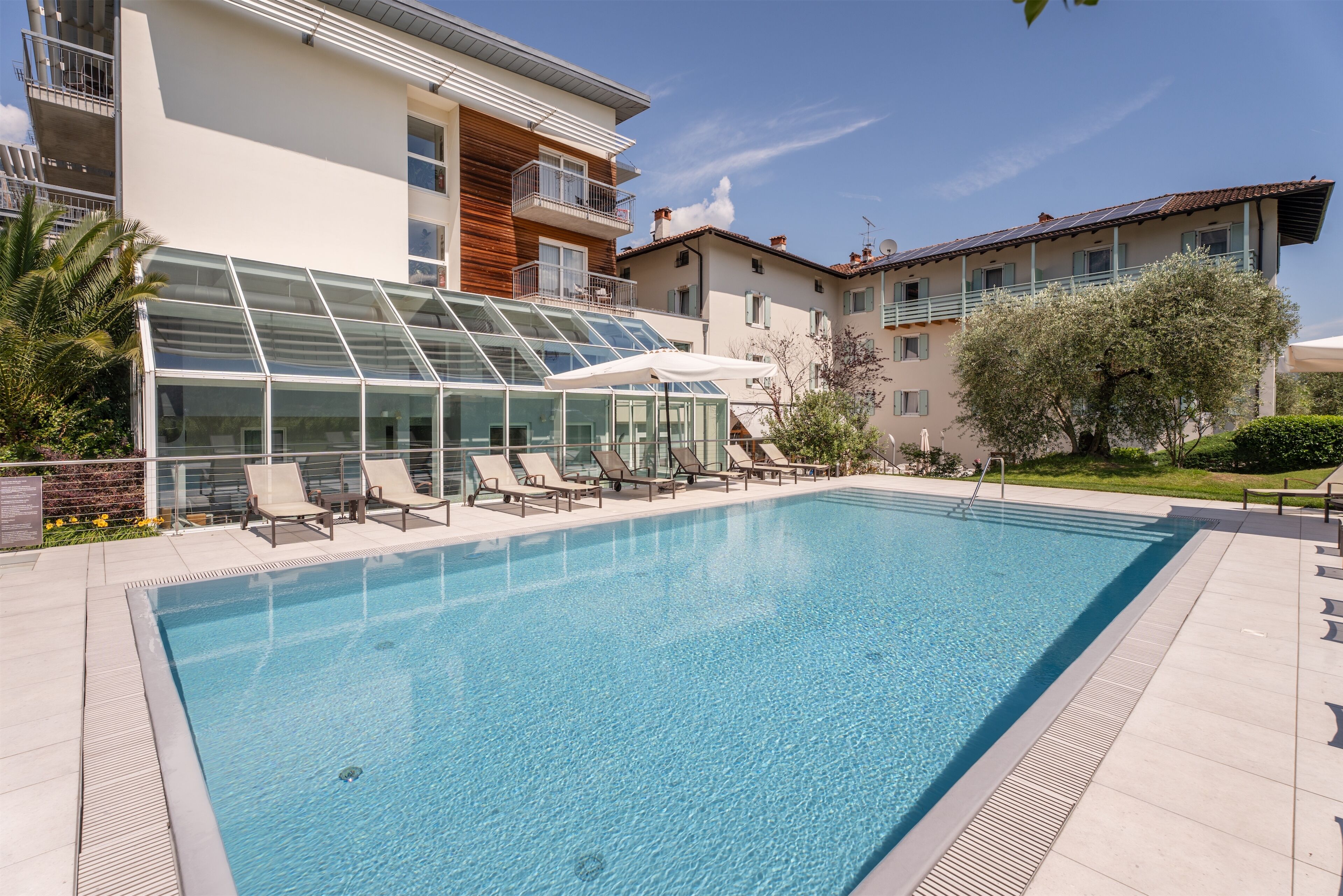 A swimming pool with lounge chairs, a glass-enclosed area, and modern buildings in the background.