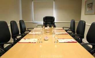 Un salón de conferencias con una larga mesa, sillas negras y copas de vino preparadas para una reunión.