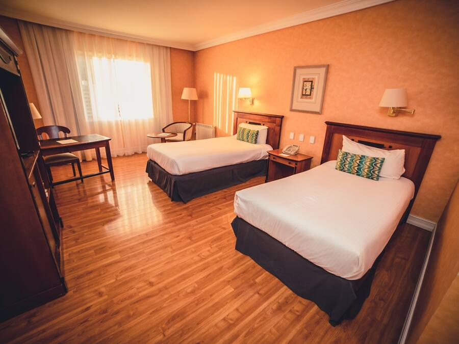 Et hotelværelse med to senge, et skrivebord og en stol.