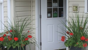 Une entrée de maison avec une porte blanche, une boîte aux lettres et deux grands pots de fleurs ornés de fleurs rouges.