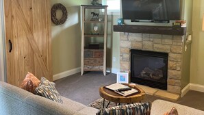 Un salon avec une cheminée, un téléviseur, une porte coulissante de style grange et une bibliothèque.