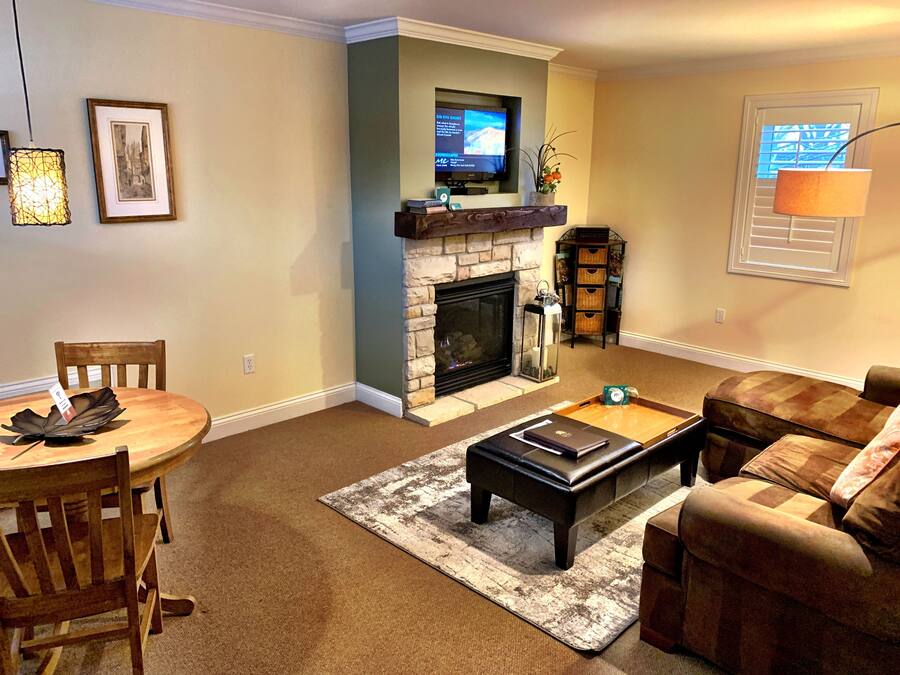 Una sala de estar con chimenea, un televisor montado encima, una mesa de comedor con sillas y un sofá.