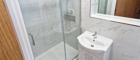 A modern bathroom with a glass shower enclosure, a white sink, and a wooden door.