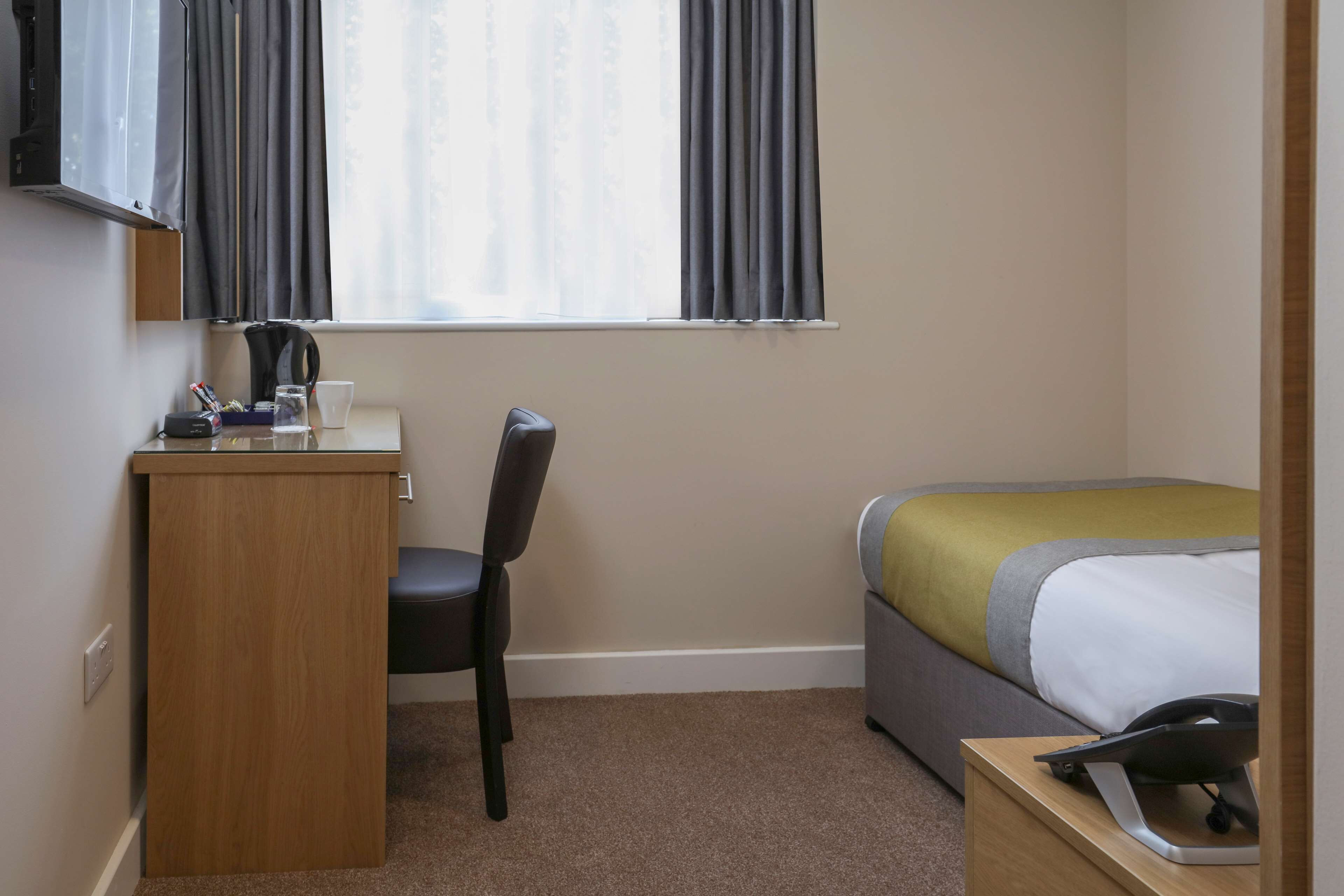 Habitación de hotel con escritorio, silla, cama y ventana con cortinas.