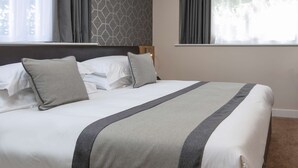 A neatly made bed with a grey and white striped bedspread, a headboard with a geometric pattern, and a window with grey curtains. -  Best Western Northfields Ealing Hotel-Opposite Northfield Station -Piccadilly line (London)