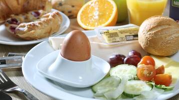 Ein Frühstücksteller mit Eiern, Brot, Tomaten, Gurken und einem Glas Orangensaft.