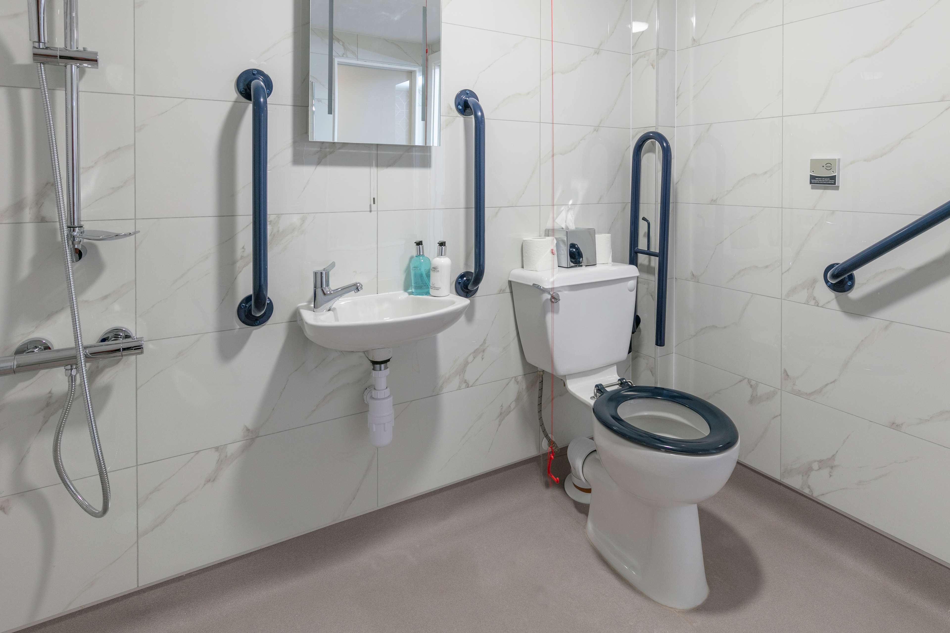 A bathroom with a white sink, toilet, and shower. There are grab bars installed for support.