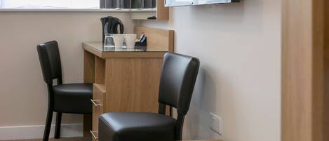 A small, modern room with a desk and two chairs, a television mounted above the desk, and a window with curtains.