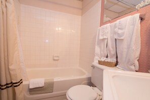A bathroom with a bathtub, toilet, and a mirror. There are towels hanging on the wall and a basket on the toilet. - Biltmore Suites Hotel (Baltimore)