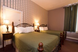 A hotel room with two beds, each with a wooden headboard and a green bedspread. There are two bedside tables with lamps, and a window with curtains. - Biltmore Suites Hotel (Baltimore)