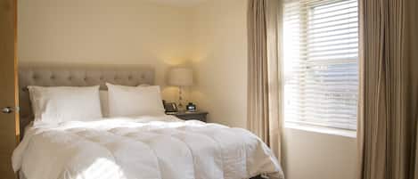 Un dormitorio con una cama grande, una mesita de noche con lámpara y una ventana con cortinas.