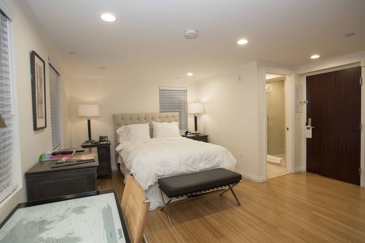 A bedroom with a bed, bedside tables, a bench, a desk, and a map.