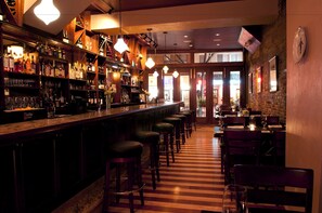 Un bar con una barra larga, varios taburetes y piso a rayas.