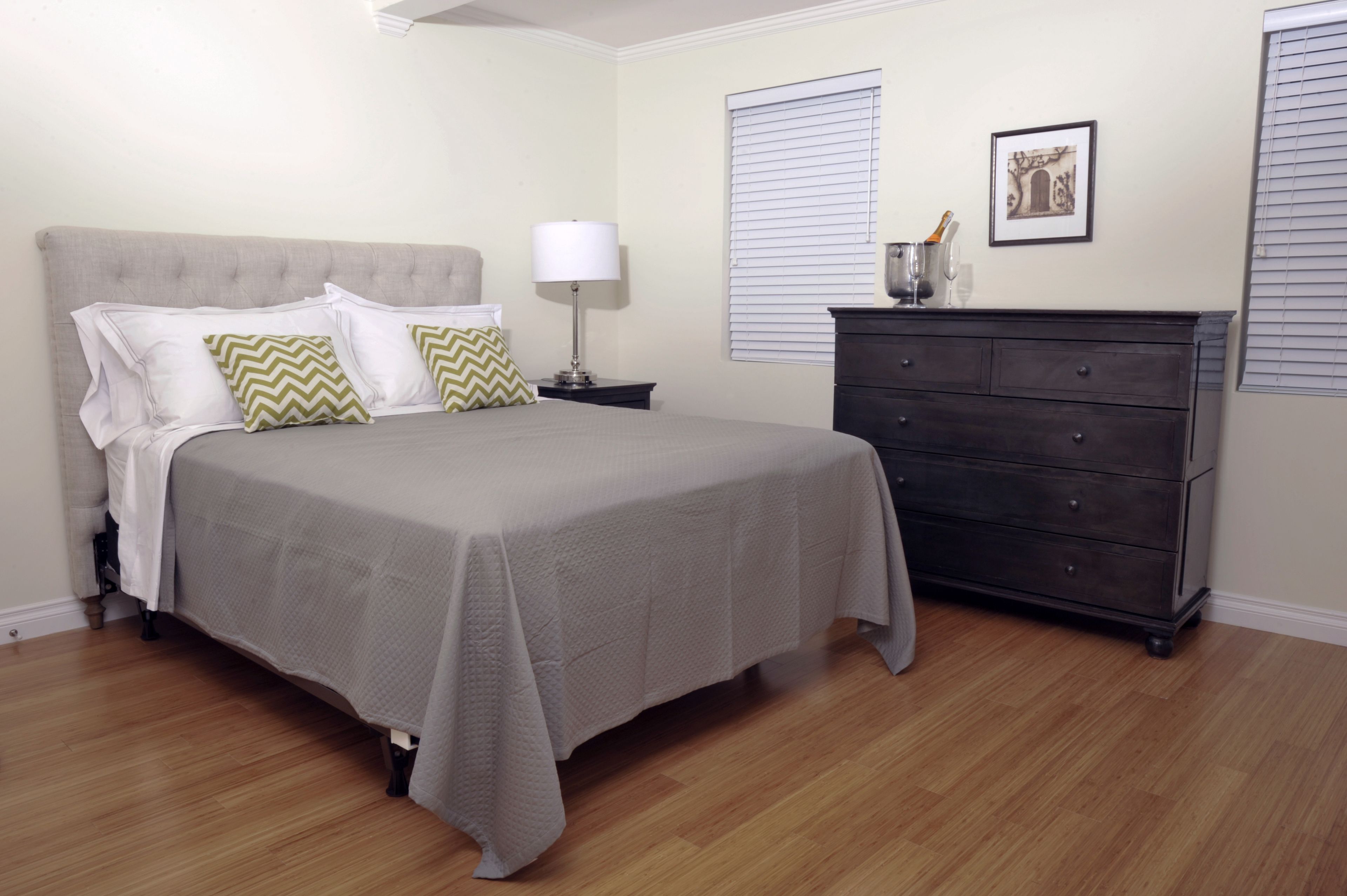 A bedroom with a bed, nightstand, dresser, and a window with blinds.