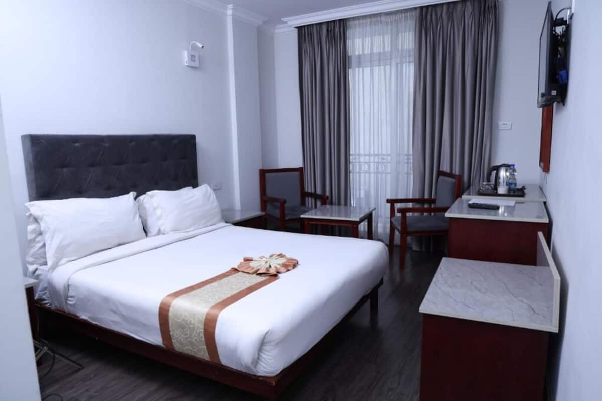 A hotel room with a bed, a desk, two chairs, a television, and a window with curtains.