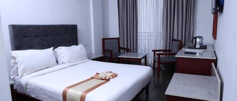 A hotel room with a bed, a desk, two chairs, a television, and a window with curtains.