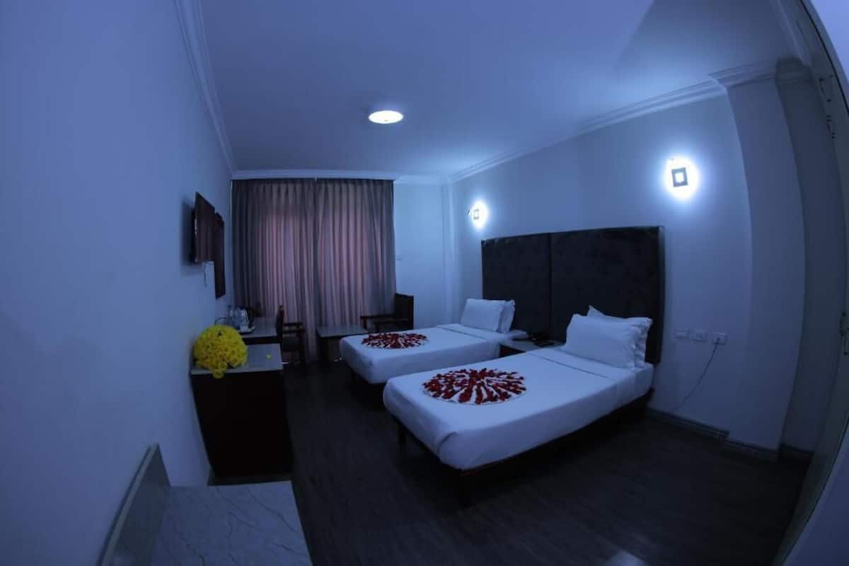 A hotel room with two beds, a desk, a chair, and a small table.