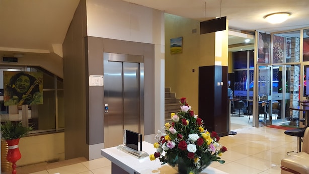 A reception area with a modern elevator, a desk with a laptop, and a floral arrangement. - Trinity Hotel (Addis Ababa)