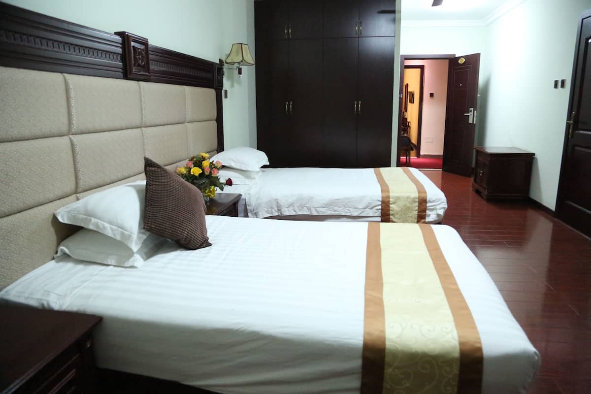A hotel room with two beds, a wardrobe, a nightstand, and a lamp.