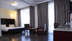 A hotel room with a bed, two chairs, a desk, and a large window with curtains. - Trinity Hotel (Addis Ababa)