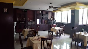 A restaurant interior with multiple tables and chairs, a ceiling fan, and a wine rack with bottles. - Trinity Hotel (Addis Ababa)