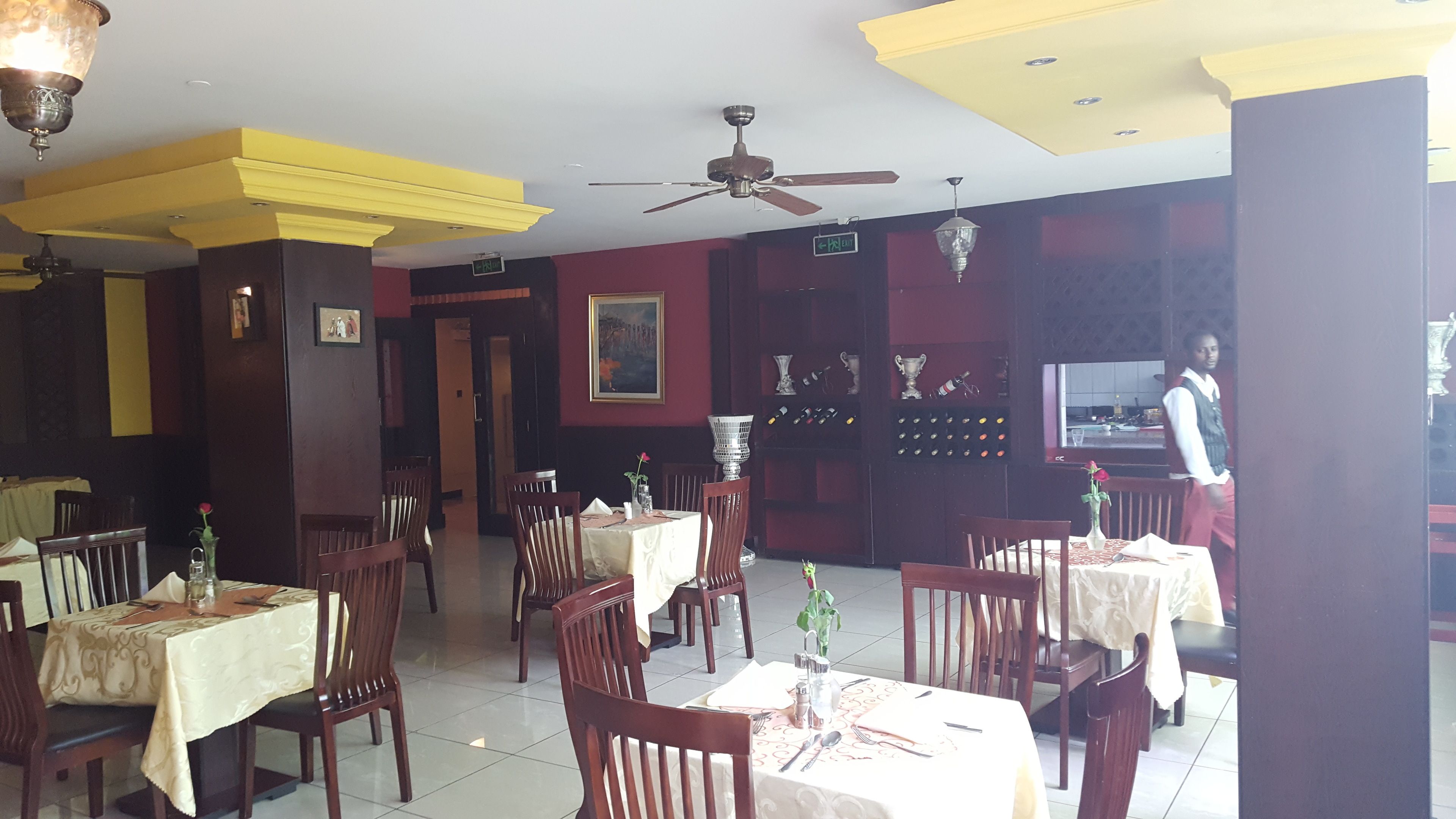 Un ristorante con diversi tavoli e sedie, una ventola a soffitto e un cameriere vicino all'ingresso.