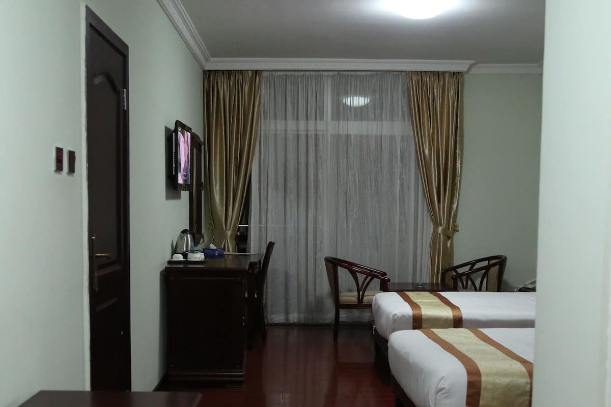 A hotel room with a wooden floor, a ceiling fan, a bed with a brown and white bedspread, a desk with a chair, and a television on the wall.