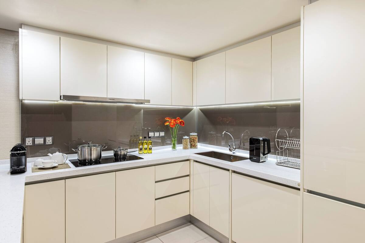 Una cocina moderna con armarios blancos, una campana extractora de acero inoxidable, un fregadero y diversos electrodomésticos.