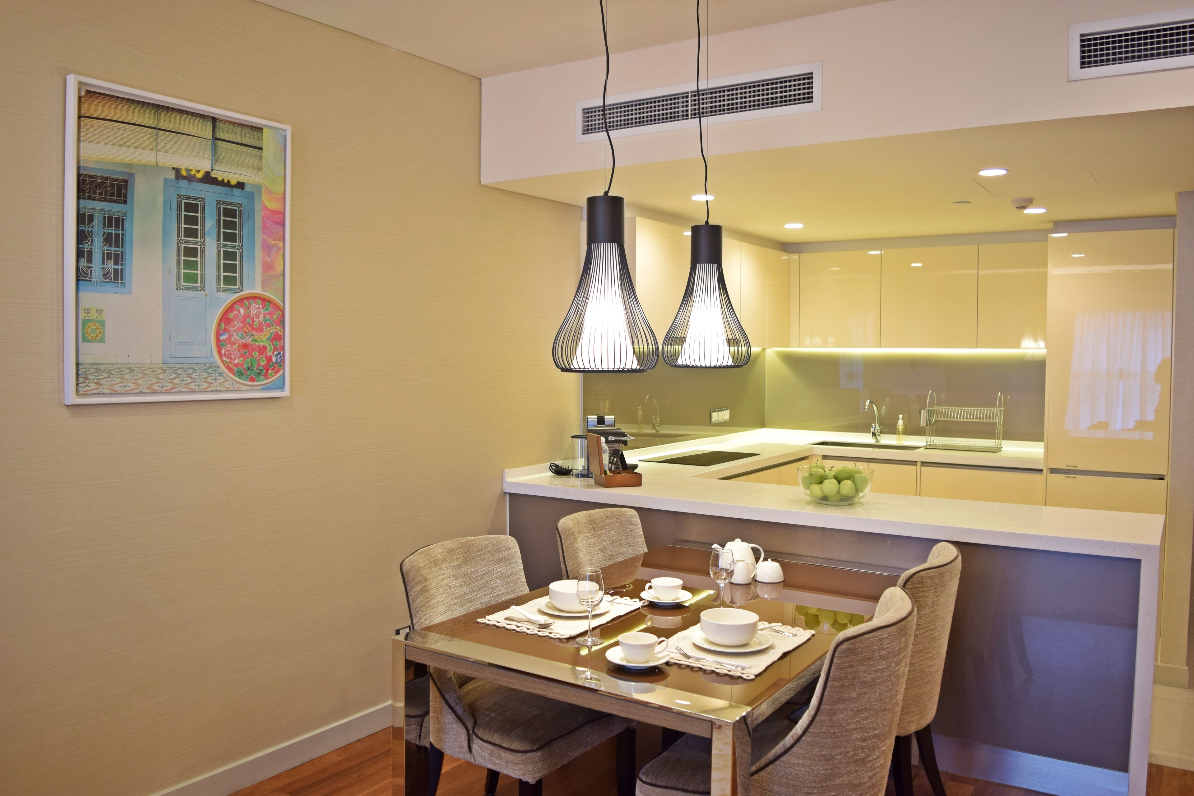 A modern dining area with a wooden table set for four, a kitchen in the background, and a decorative wall piece.