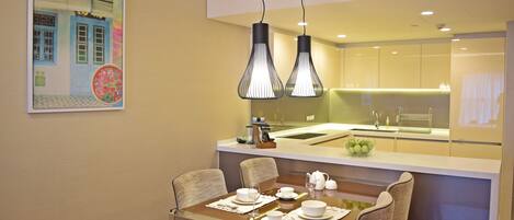 A modern dining area with a wooden table set for four, a kitchen in the background, and a decorative wall piece.