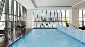 An indoor swimming pool with clear glass walls, wooden flooring, and a view of the cityscape. - Ascott Sentral Kuala Lumpur (Kuala Lumpur)