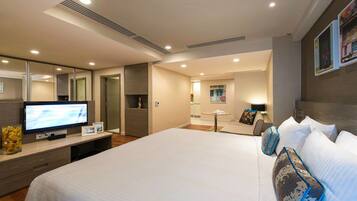 A modern hotel room with a large bed, a flat-screen TV, a desk, and a bathroom visible through an open door.