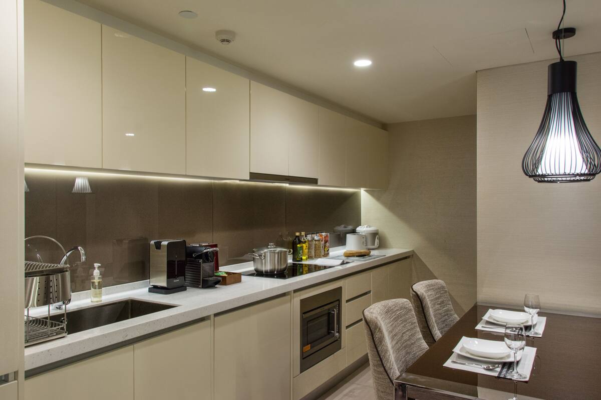 Una cocina moderna con horno empotrado, cafetera y zona de comedor con mesa para dos.