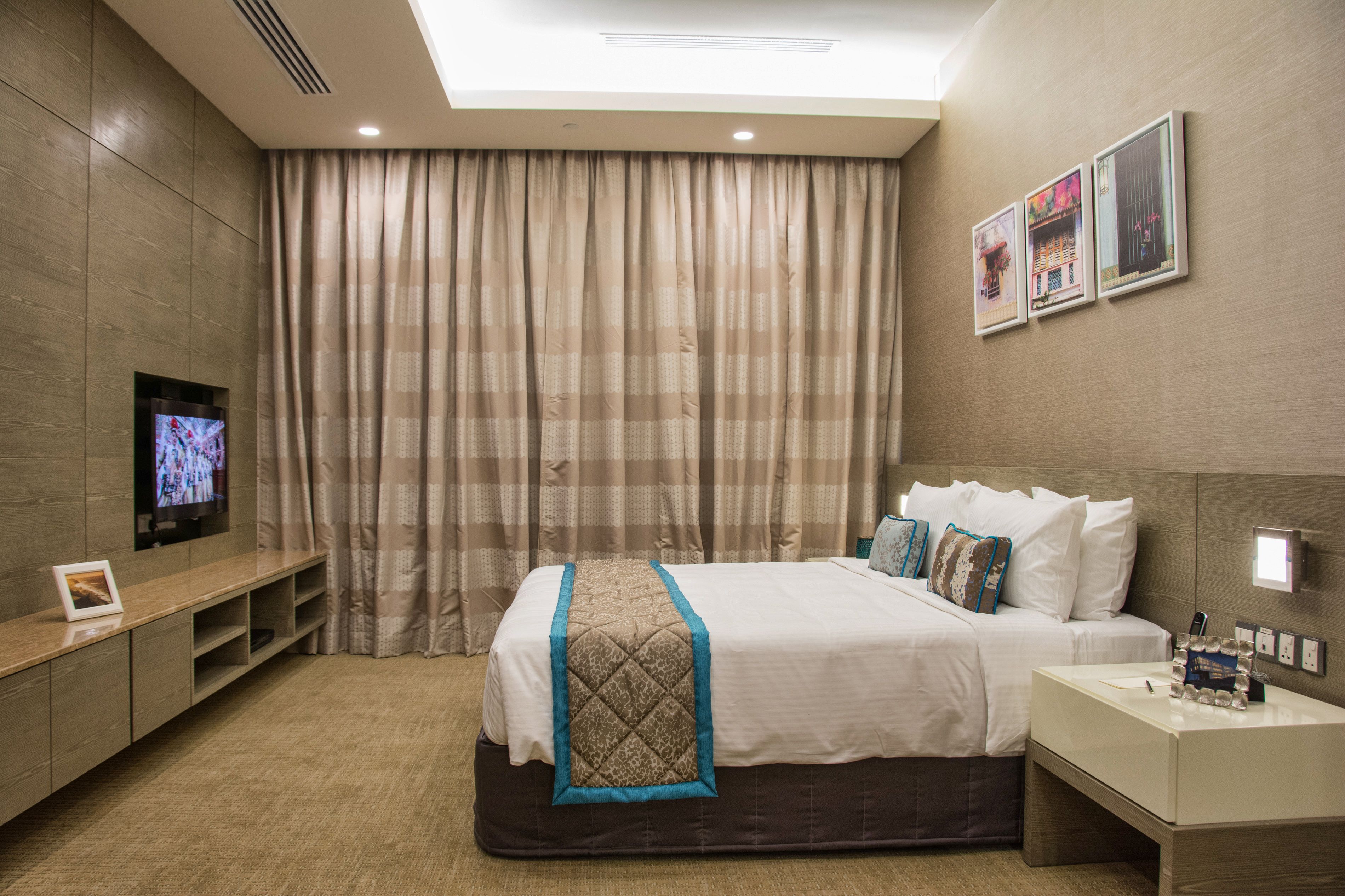 Una camera d'albergo con un letto, una televisione, un comodino e un'ampia finestra con tende.