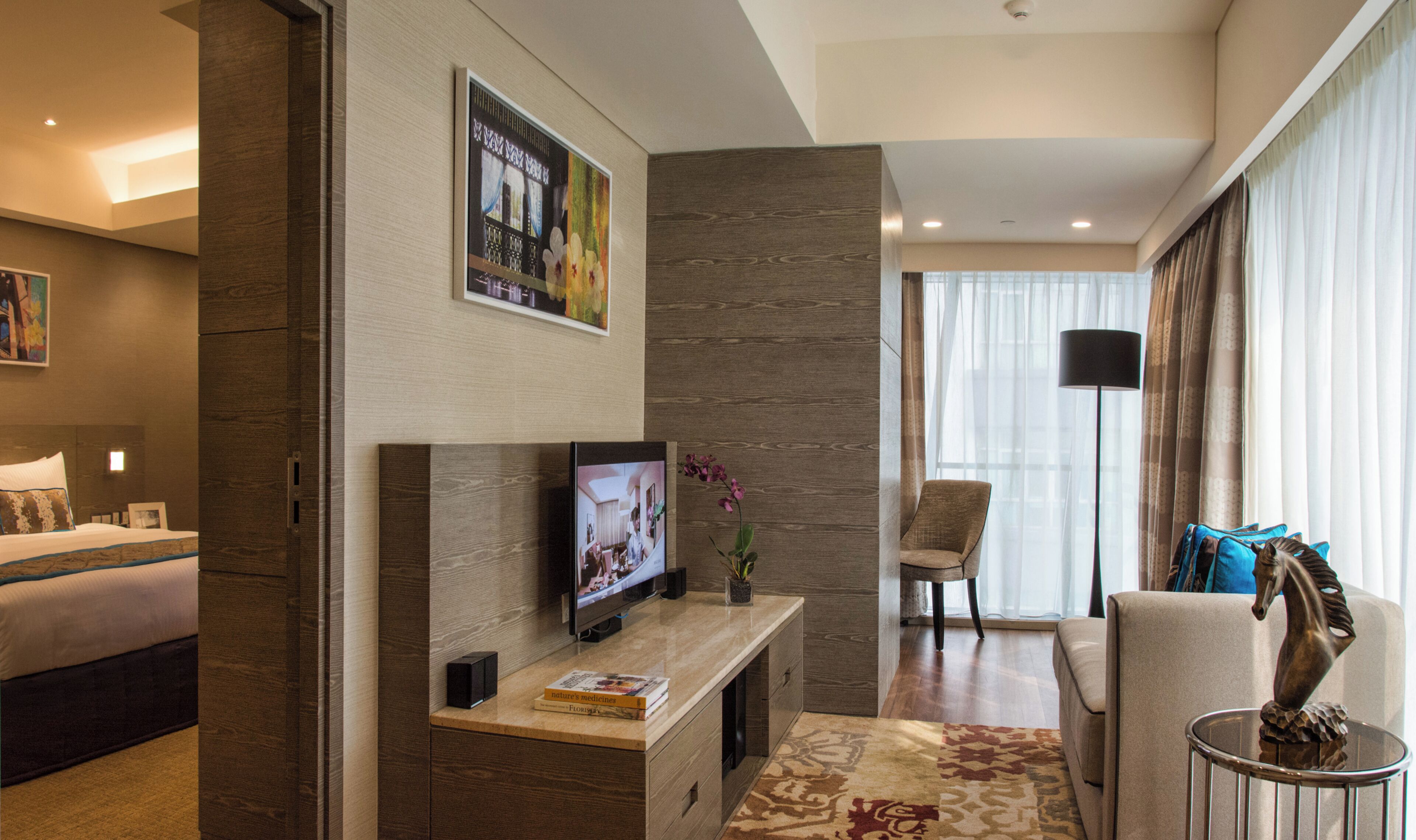 Una habitación de hotel con una cama, un televisor sobre un mueble de madera, una silla, un sofá y un ventanal con cortinas.