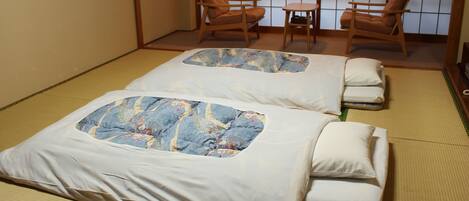 Two tatami mat beds with pillows, a small table, and two wooden chairs in a traditional Japanese room.